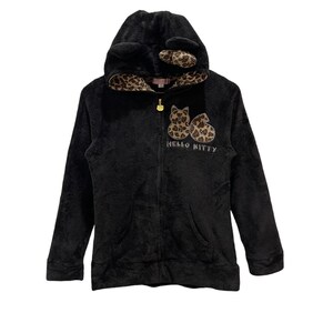 Peut inclure: Sweat-shirt &agrave; capuche noir en polaire avec un motif Hello Kitty. La capuche a des oreilles de chat et une doublure &agrave; imprim&eacute; l&eacute;opard.