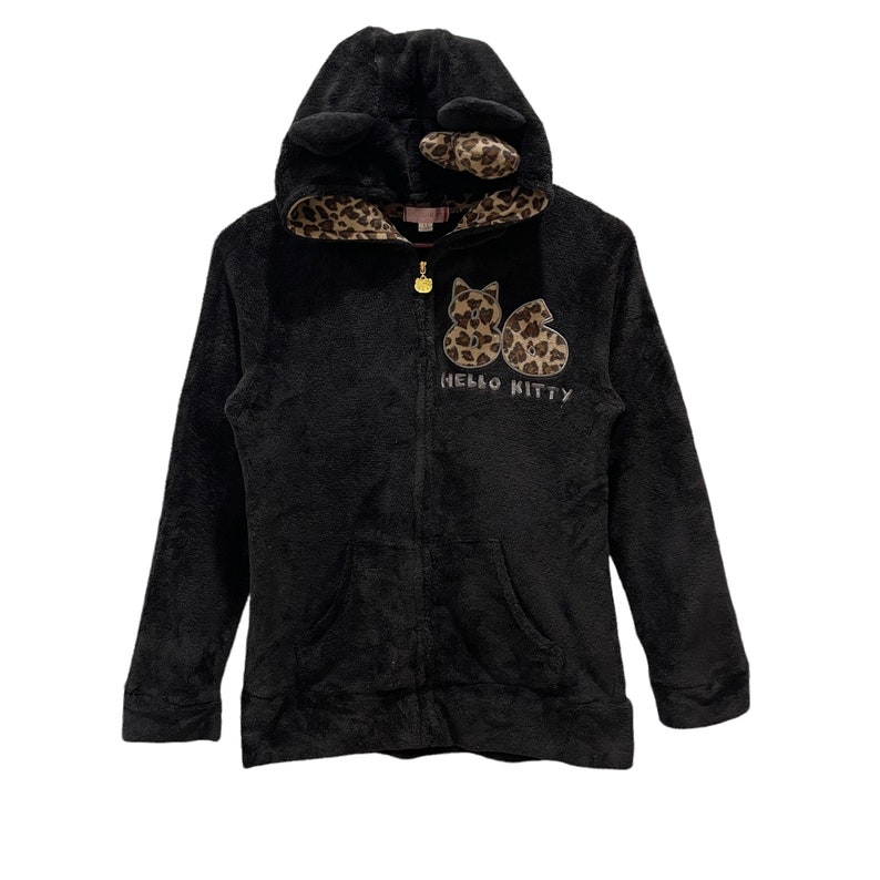 Peut inclure: Sweat-shirt &agrave; capuche noir en polaire avec un motif Hello Kitty. La capuche a des oreilles de chat et une doublure &agrave; imprim&eacute; l&eacute;opard.