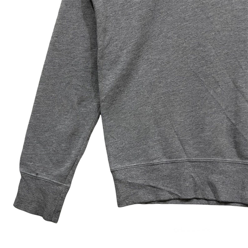 May include: Close-up of a gray sweatshirt. The image shows the sleeve and part of the body of the garment. The fabric appears to be a soft, knit material. The cuff and hem are ribbed.