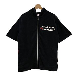 May include: Black hooded zip-up short-sleeved shirt. The shirt features the text "HELLO KITTY x MY MELODY" in white and red. The shirt is hanging on a wooden hanger.