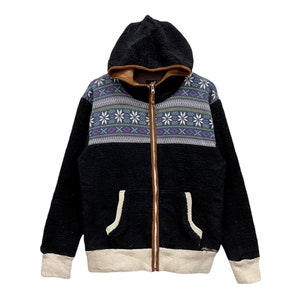 Puede incluir: Chaqueta de forro polar con capucha negra con canesú estampado con copos de nieve y diseños geométricos en morado, verde y blanco. La chaqueta tiene cremallera marrón, forro de capucha y ribete de bolsillo, con puños y dobladillo beige.