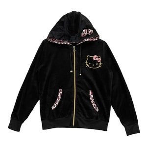 Pode incluir: Casaco de moletom preto de veludo com z&iacute;per dourado e um gr&aacute;fico de Hello Kitty na frente. O capuz &eacute; forrado com uma estampa de leopardo rosa e preto.