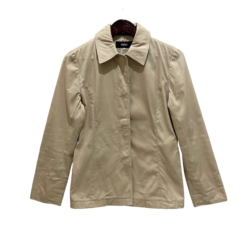 May include: A tan jacket with a collared neckline and long sleeves. The jacket has a button-up front and is hanging on a wooden hanger. The brand name "NEO" is visible on the label.