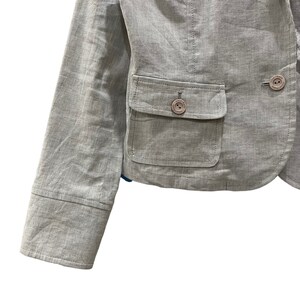 Puede incluir: Una blazer gris claro con un corte entallado. La chaqueta presenta solapas con muescas, dos bolsillos delanteros y botones con un logotipo. Las mangas tienen un detalle de pu&ntilde;o abotonado. La blazer est&aacute; hecha de una tela texturizada.