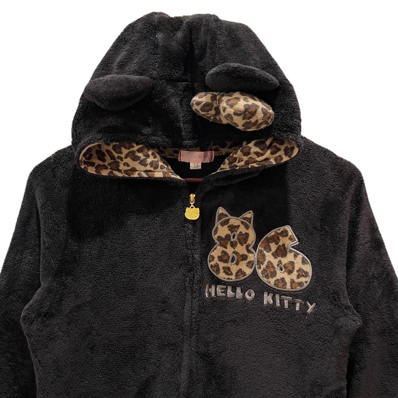 Peut inclure: Sweat-shirt &agrave; capuche noir en polaire avec une doublure &agrave; imprim&eacute; l&eacute;opard et un motif Hello Kitty. La capuche est orn&eacute;e d'oreilles de chat noires et d'une bordure &agrave; imprim&eacute; l&eacute;opard.