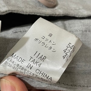 Puede incluir: Primer plano de una etiqueta de ropa con texto japon&eacute;s y las palabras "MADE IN CHINA". La etiqueta enumera los porcentajes de composici&oacute;n de la tela: 54%, 42% y 4%. La etiqueta es blanca con texto negro.