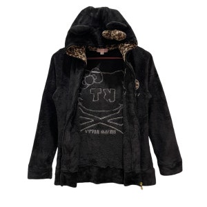 Peut inclure: Sweat-shirt &agrave; capuche noir en polaire avec un motif Hello Kitty et une doublure en imprim&eacute; l&eacute;opard. La capuche est orn&eacute;e d'oreilles de chat.