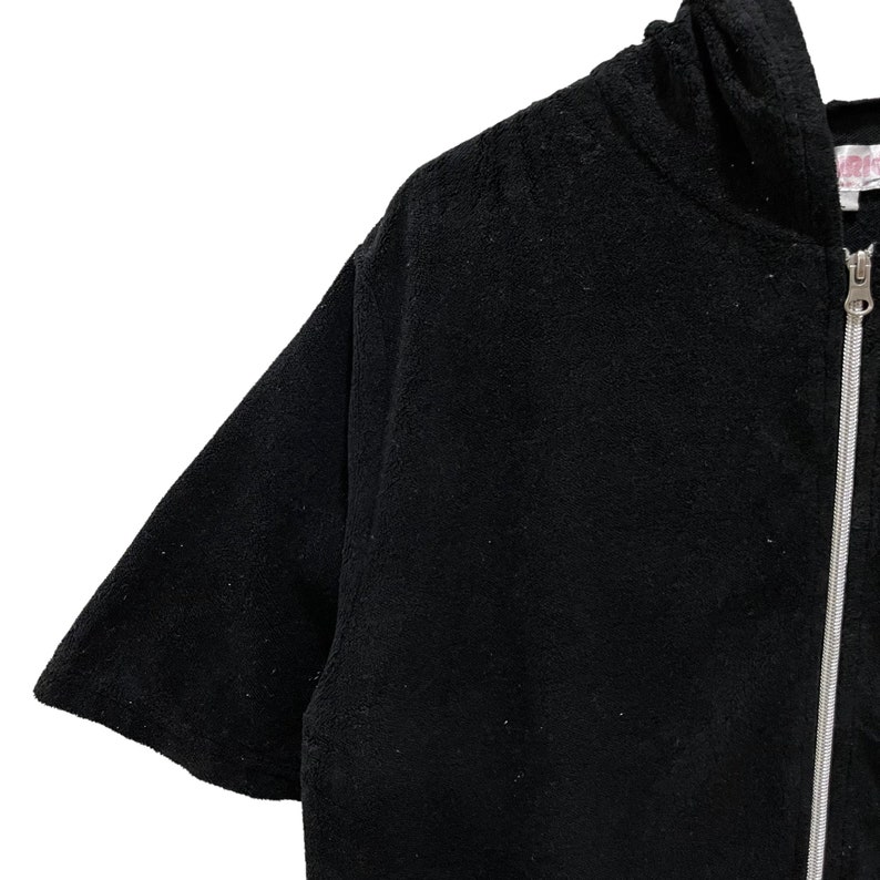 May include: Black hooded zip-up jacket with short sleeves. The jacket features a silver zipper and a soft, textured finish. The hood is visible at the top, and the sleeves are short. The jacket is made of a thick material.
