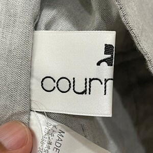 Puede incluir: Primer plano de una etiqueta de ropa blanca con el nombre de la marca "courr" en negro, fuente sans-serif. Un gr&aacute;fico negro est&aacute; encima del nombre de la marca. La etiqueta est&aacute; cosida en una tela gris. La etiqueta tambi&eacute;n tiene texto japon&eacute;s y un n&uacute;mero de tel&eacute;fono.