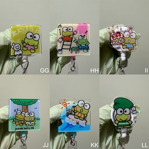 Op de afbeelding: Set van tien kleurrijke cartoon-kikkerfiguurtjes sleutelhangers. Elke sleutelhanger heeft een ander kikkerontwerp met een andere achtergrond. De sleutelhangers zijn gemaakt van helder plastic en hebben een metalen ring om sleutels aan te bevestigen.