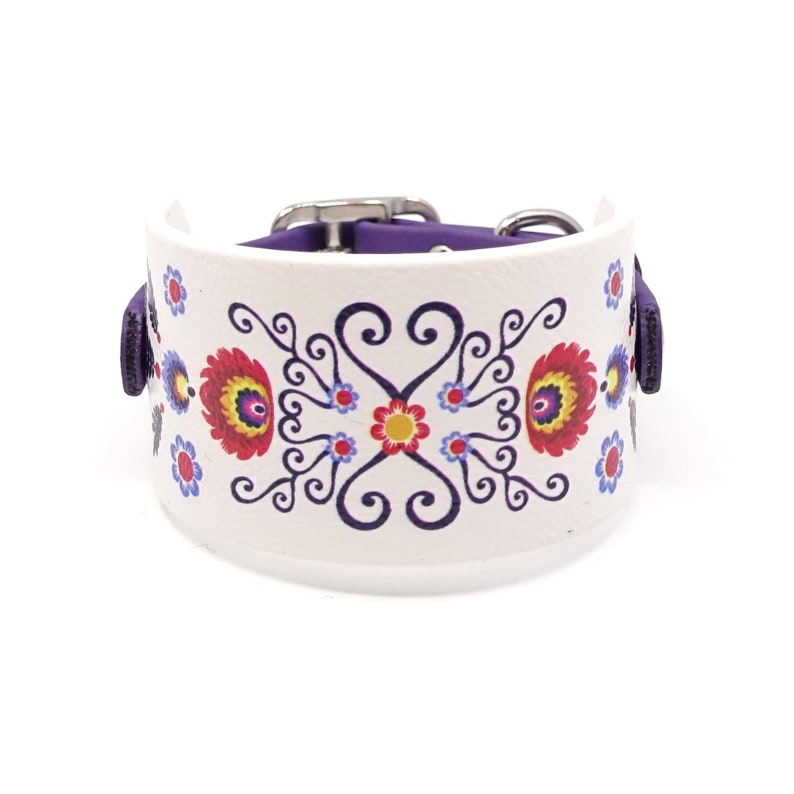 Puede incluir: Un collar de perro de cuero blanco con ribete morado y un estampado floral colorido. El collar tiene una hebilla plateada.