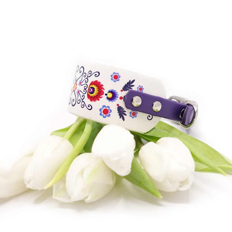 Puede incluir: Collar de perro de cuero blanco con ribete morado y un estampado floral colorido. El collar est&aacute; decorado con un dise&ntilde;o tradicional de arte popular.