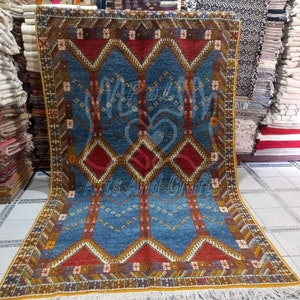 May include: A blue, red, and gold patterned rug with a geometric design. The rug has a fringe border.