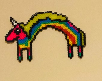 May include: A rainbow unicorn made of colorful beads. The unicorn is arched with its head and legs on the ground. The unicorn has a yellow mane and tail.