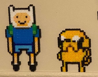 May include: A blue and white pixel art figure of Finn the Human from Adventure Time, standing next to a yellow pixel art figure of Jake the Dog.