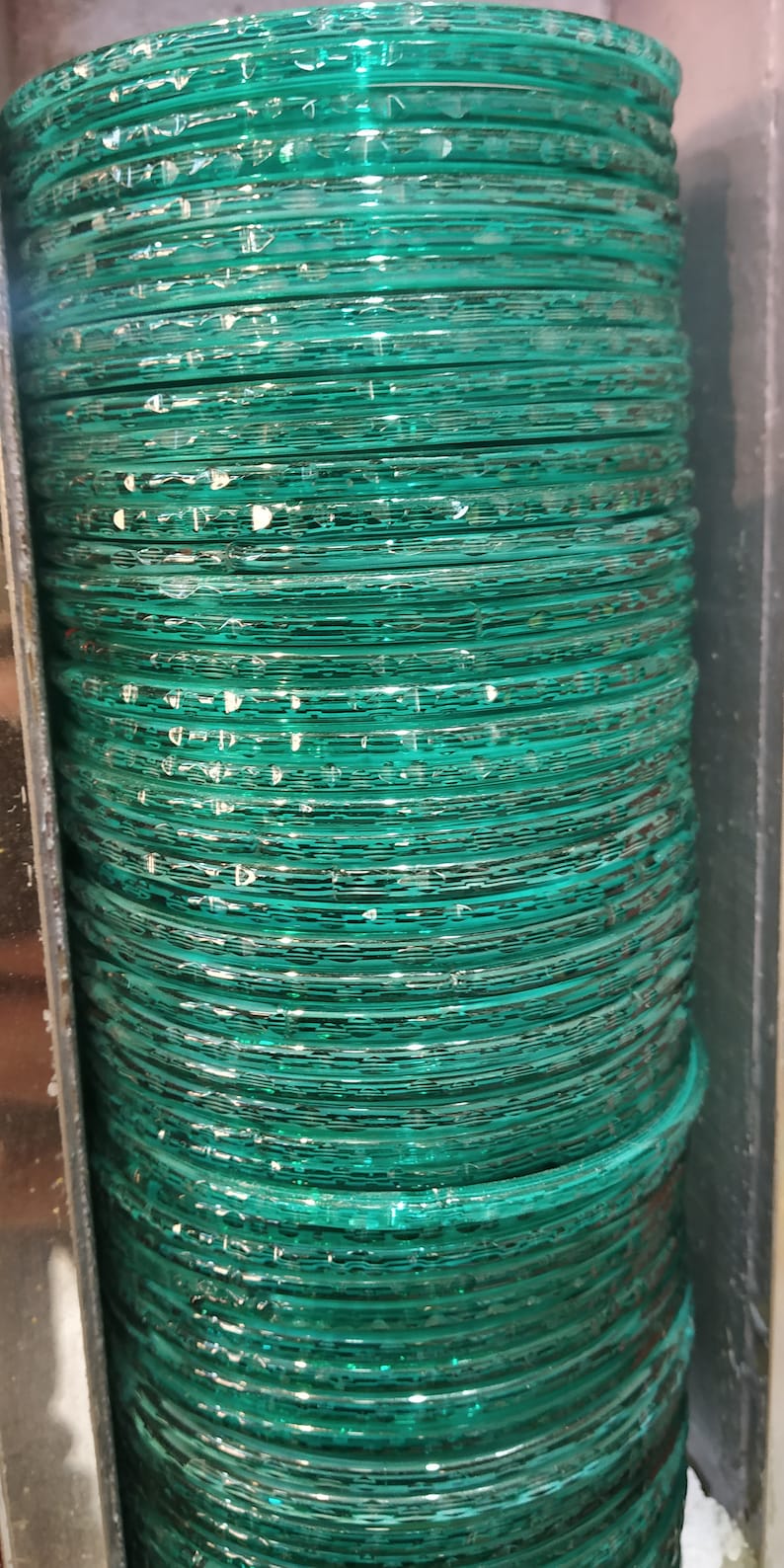 Puede incluir: Una pila de brazaletes de vidrio verde azulado. Los brazaletes son lisos y brillantes, y est&aacute;n apilados uno encima del otro.