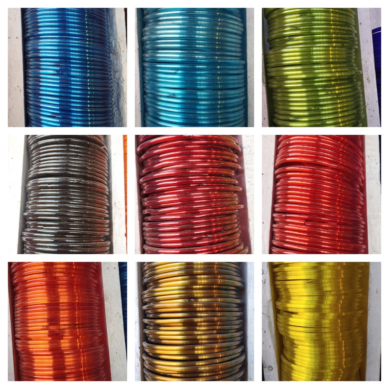 May include: A collection of colourful glass bangles stacked in rows. The bangles are in various colours, including blue, green, red, gold, and silver.