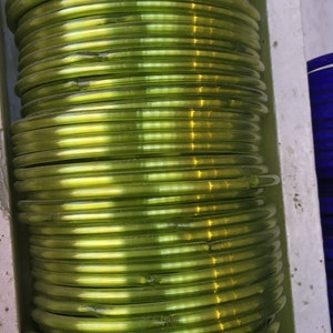 May include: A stack of green glass bangles. The bangles are shiny and have a slight iridescent quality.