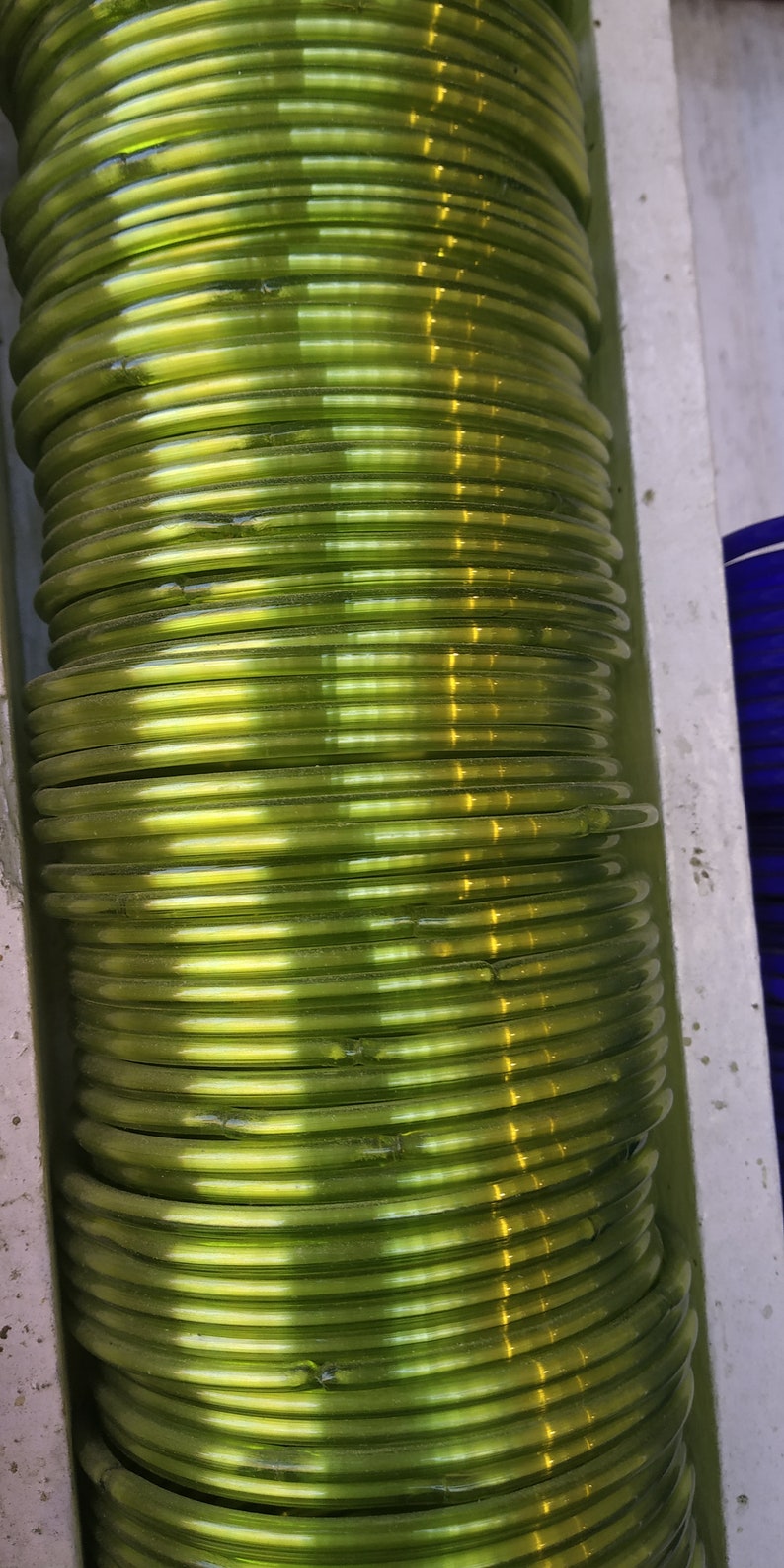 May include: A stack of green glass bangles. The bangles are shiny and have a slight iridescent quality.