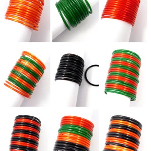 May include: A set of nine colorful bangles, including black, orange, and green. The bangles are stacked in three groups of three, with each group featuring a different color combination.