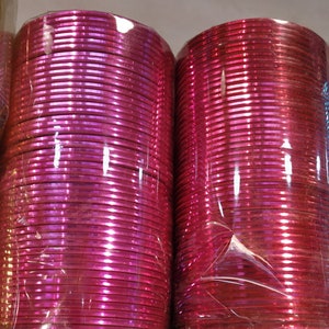 May include: A stack of pink metal bangles, wrapped in plastic, with a shiny, iridescent finish.