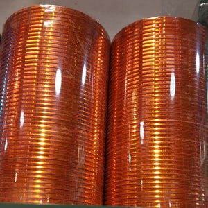May include: A stack of orange glass bangles wrapped in plastic. The bangles are shiny and have a reflective surface.