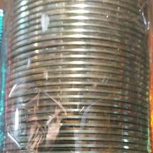 May include: A stack of silver-colored bangles wrapped in clear plastic packaging. The bangles are stacked in a circular pattern and have a shiny finish.