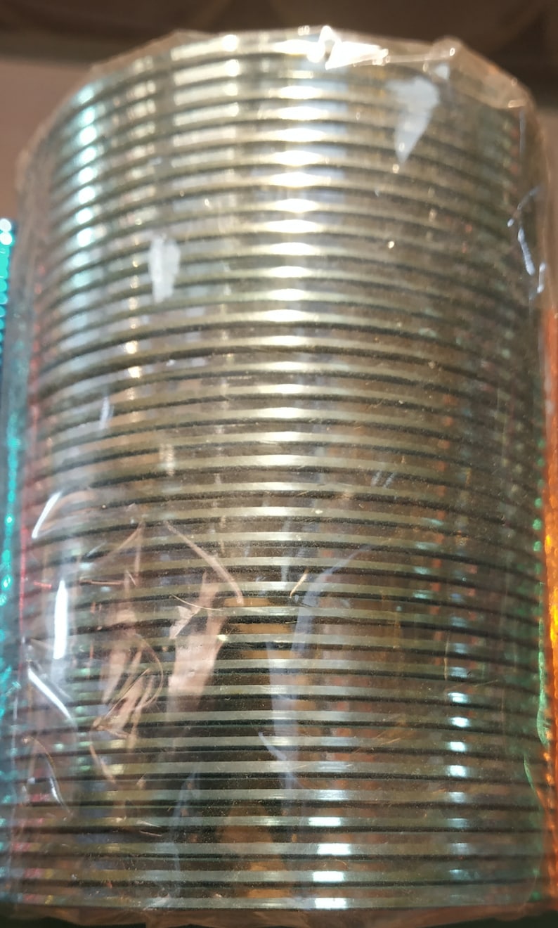May include: A stack of silver-colored bangles wrapped in clear plastic packaging. The bangles are stacked in a circular pattern and have a shiny finish.