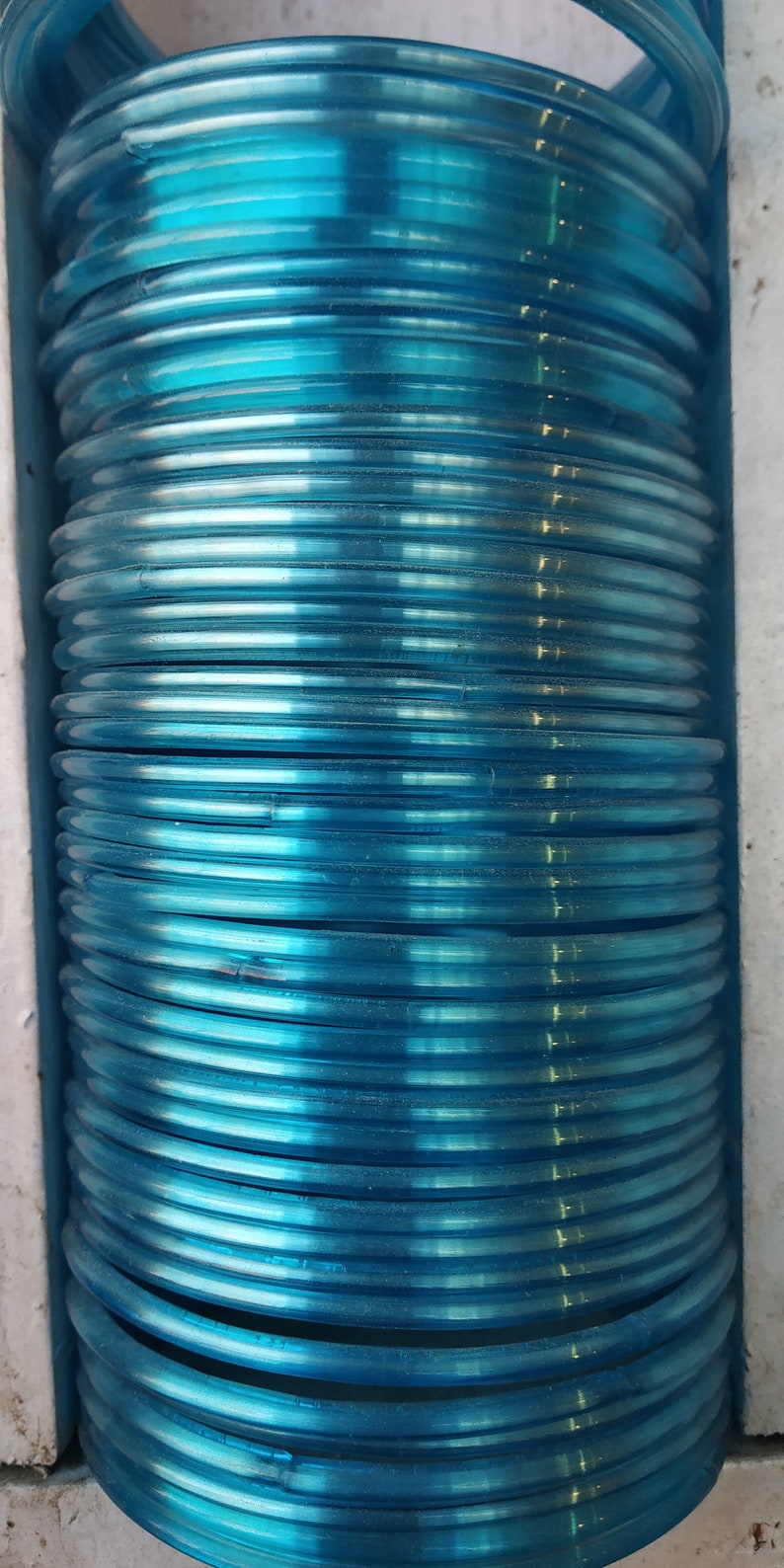 May include: A stack of light blue plastic bangles. The bangles are stacked on top of each other and are arranged in a circular pattern.