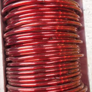 May include: A stack of red glass bangles. The bangles are shiny and have a slight iridescent quality.