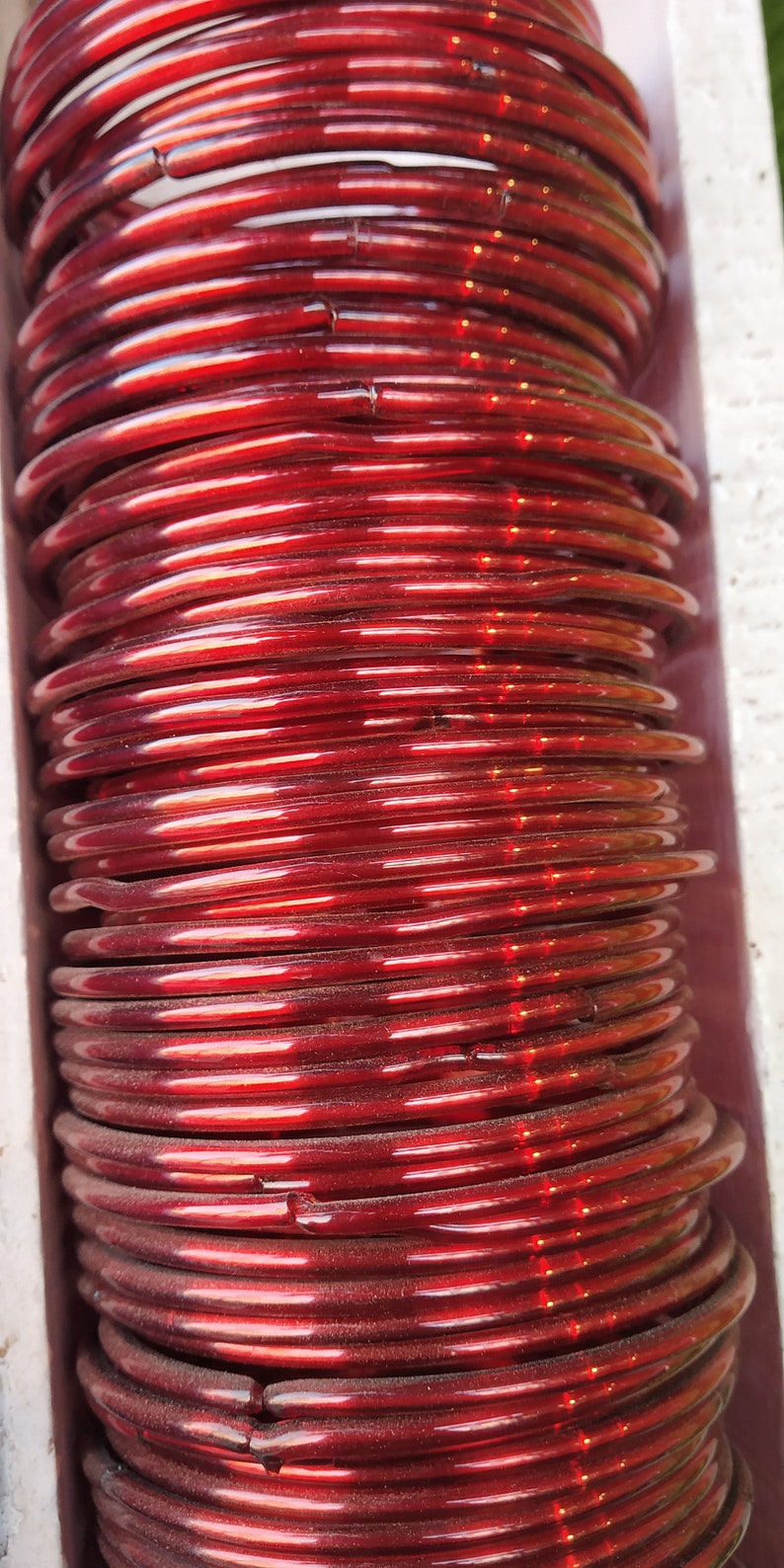May include: A stack of red glass bangles. The bangles are shiny and have a slight iridescent quality.