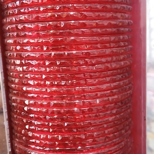 Puede incluir: Una pila de brazaletes de vidrio rojo con un patr&oacute;n de diamante. Los brazaletes est&aacute;n apilados uno encima del otro y est&aacute;n dispuestos en una l&iacute;nea vertical.