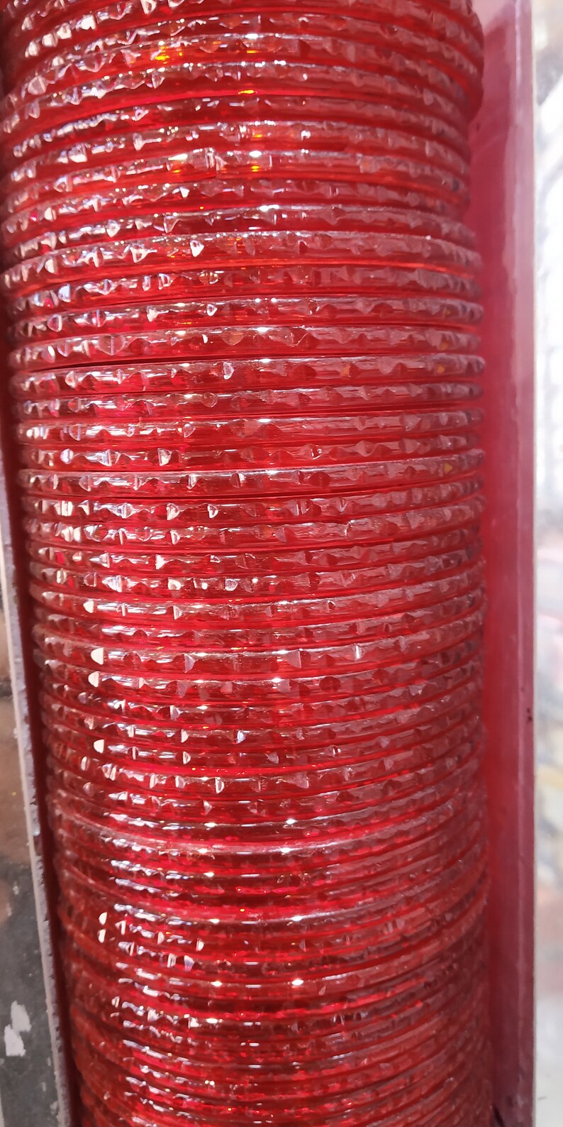 Puede incluir: Una pila de brazaletes de vidrio rojo con un patr&oacute;n de diamante. Los brazaletes est&aacute;n apilados uno encima del otro y est&aacute;n dispuestos en una l&iacute;nea vertical.