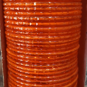 Puede incluir: Una pila de brazaletes de pl&aacute;stico naranja. Los brazaletes son transl&uacute;cidos y tienen un acabado brillante.
