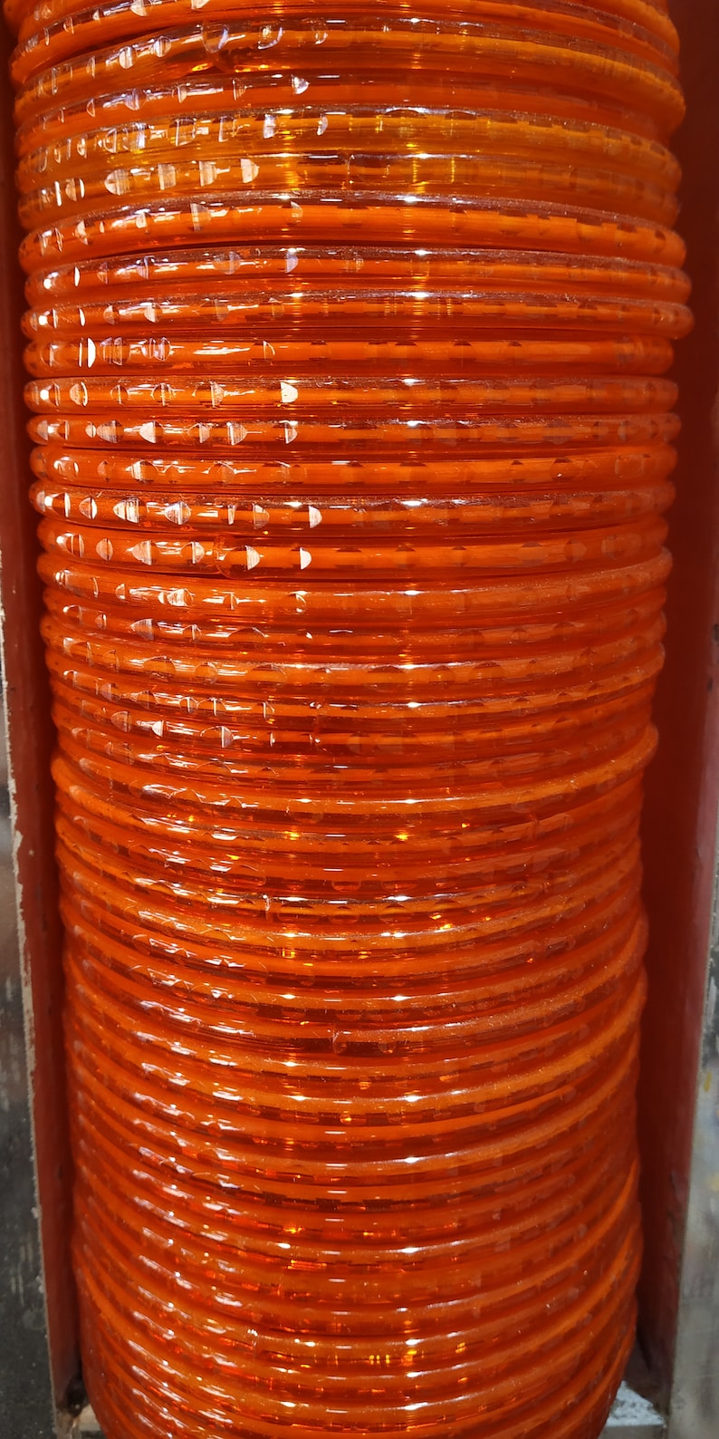 Puede incluir: Una pila de brazaletes de pl&aacute;stico naranja. Los brazaletes son transl&uacute;cidos y tienen un acabado brillante.