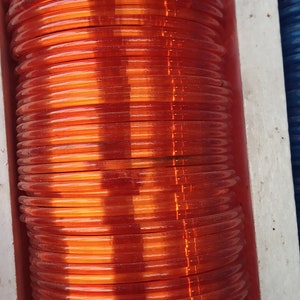 May include: A stack of orange plastic bangles. The bangles are stacked on top of each other and are arranged in a vertical line.
