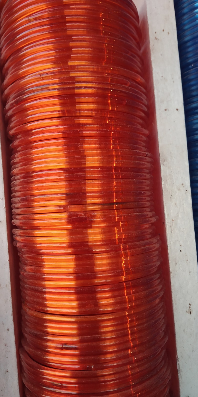 May include: A stack of orange plastic bangles. The bangles are stacked on top of each other and are arranged in a vertical line.