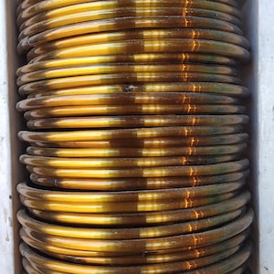 May include: A stack of gold-coloured bangles, each with a slightly different shade of brown. The bangles are arranged in a circular pattern, creating a visually appealing display.