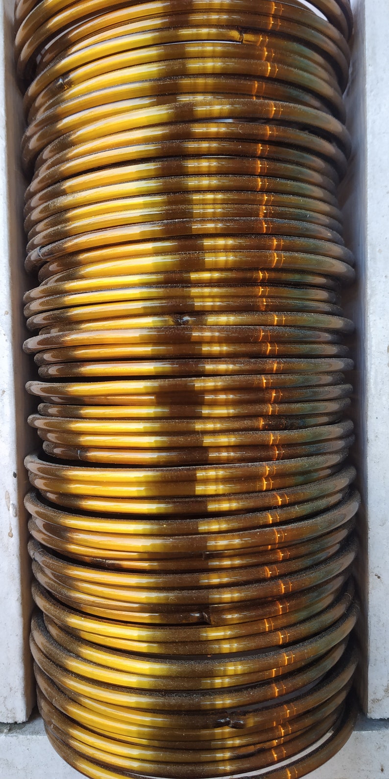 May include: A stack of gold-coloured bangles, each with a slightly different shade of brown. The bangles are arranged in a circular pattern, creating a visually appealing display.