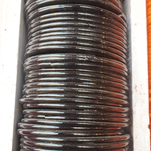 May include: A stack of black bangles, probably made of glass or plastic, arranged in a vertical column. The bangles are shiny and have a slight sheen.
