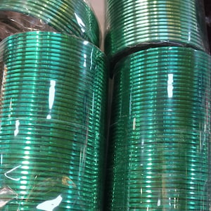 May include: A stack of green glass bangles wrapped in plastic. The bangles are shiny and have a metallic finish.