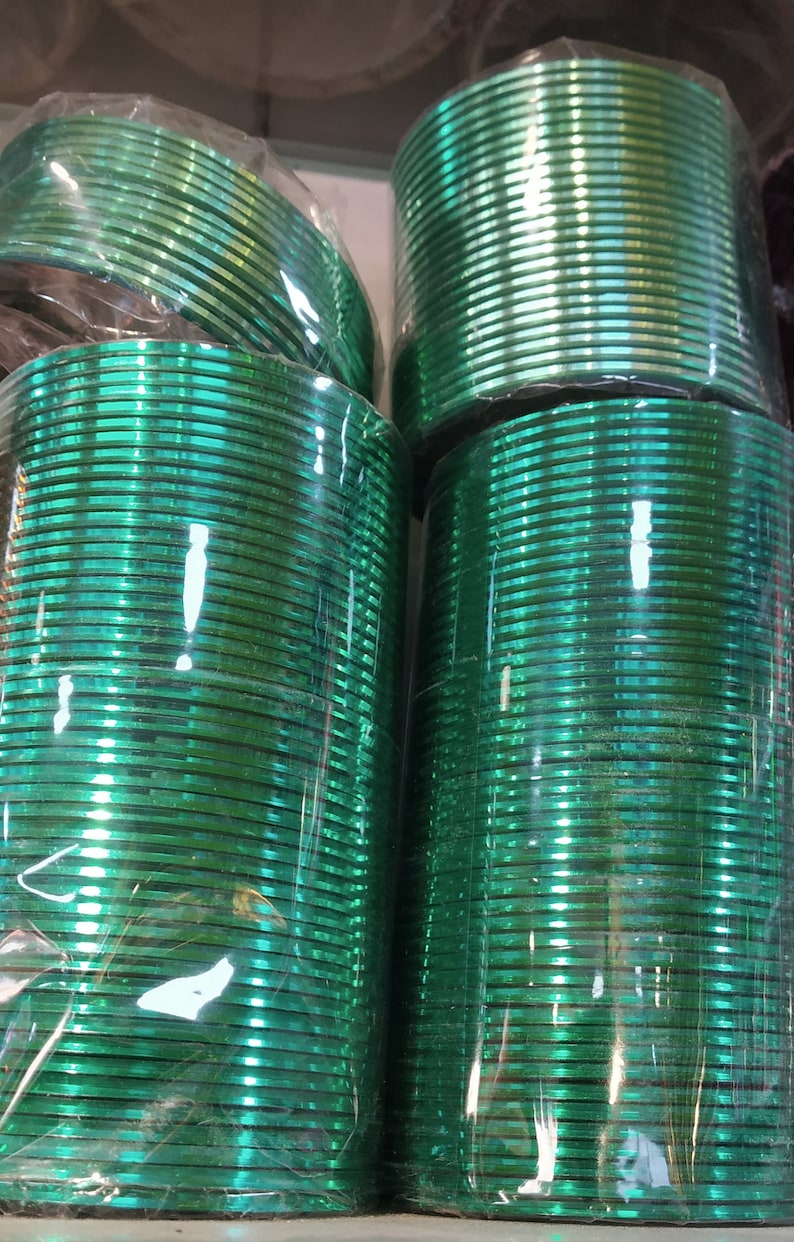 May include: A stack of green glass bangles wrapped in plastic. The bangles are shiny and have a metallic finish.