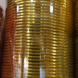 May include: A stack of gold-colored bangles wrapped in clear plastic. The bangles are shiny and have a metallic finish.