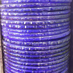 Puede incluir: Una pila de brazaletes de vidrio morado con una superficie texturizada.