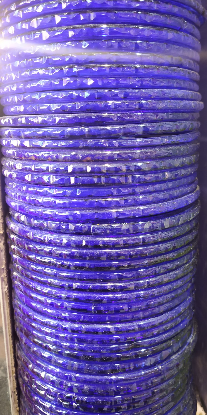 Puede incluir: Una pila de brazaletes de vidrio morado con una superficie texturizada.
