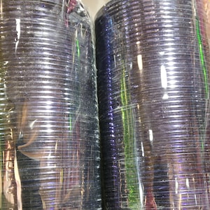 May include: Two stacks of iridescent purple bangles wrapped in clear plastic. The bangles are stacked on top of each other and are ready to be sold.