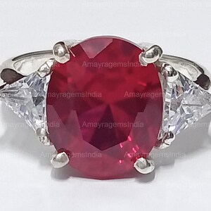Peut inclure: Une bague en argent avec une grande pierre rouge ovale et deux petites pierres blanches triangulaires de chaque côté.