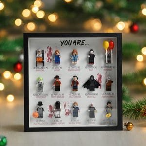 May include: A black framed shadow box with a white background and a title that reads "You Are..."  The box contains 16 miniature Lego figures of horror movie characters. Each figure is labeled with a description, such as "As Intelligent as Hannibal" or "As Funny as Chucky".