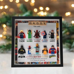 May include: A framed artwork featuring Lego superhero figures, including Thor, Hulk, Deadpool, Captain America, Hawkeye, Batman, Spiderman, Iron Man, Wolverine, and Superman. The text reads "DADDY, You are..." and "You are our favorite superhero!"