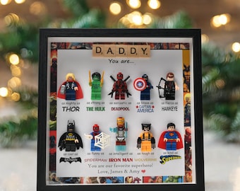 May include: A framed artwork with Lego superhero figures, such as Thor, Hulk, Deadpool, Captain America, Hawkeye, Batman, Spiderman, Iron Man, Wolverine, and Superman. The text reads "DADDY, You are..." and "You are our favourite superhero!"